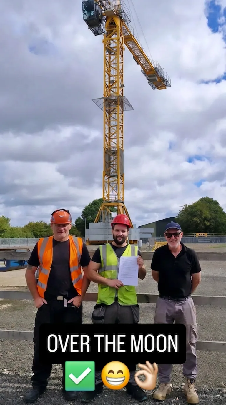 Student holding his certificate with two instructors in front of a yellow tower crane