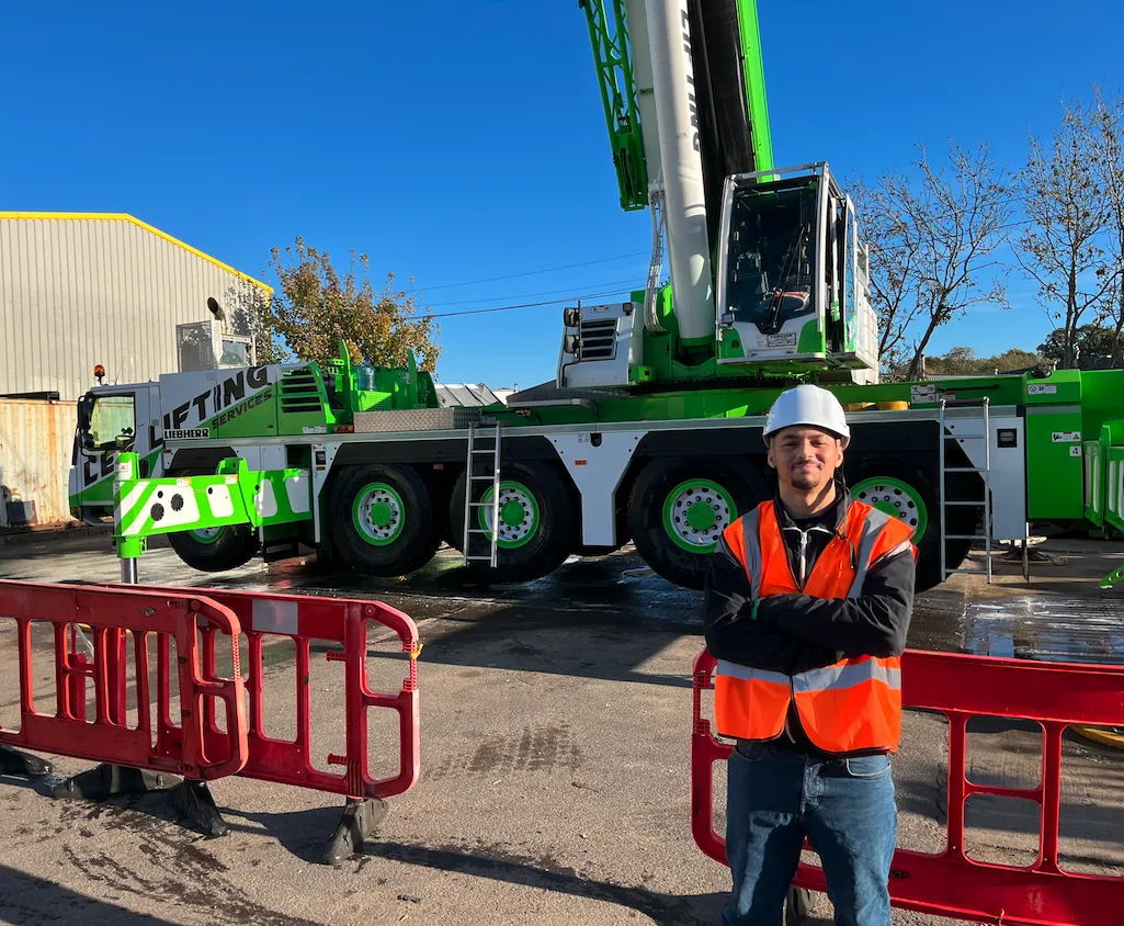 Student in a hi vis vest and white helmet standing in front of a green mobile crane